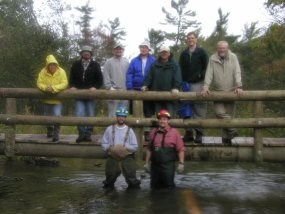 A group of volunteers stand on and below a completed bridge over a creek.