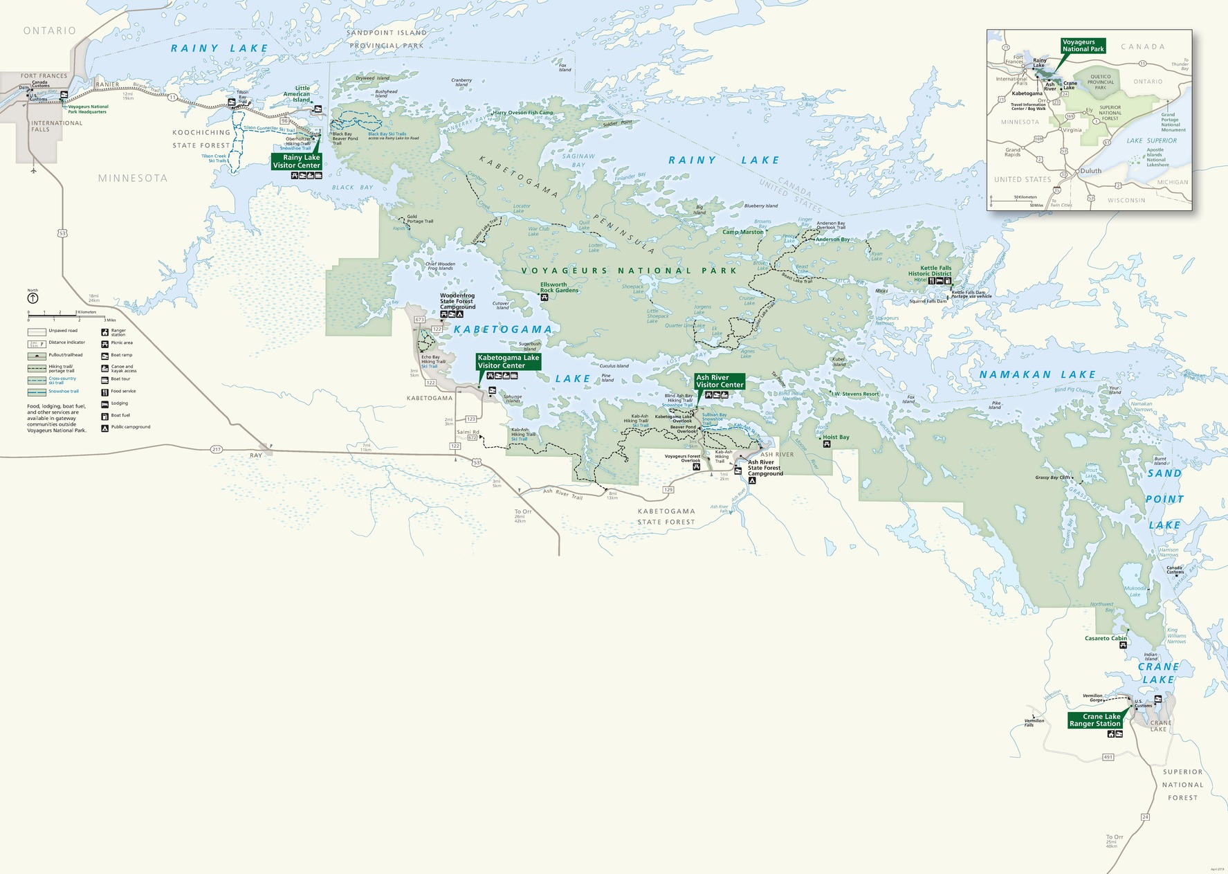 Park map of Voyageurs National Park in Minnesota. The park shown in light green, sprawls across the map from the top of the page to the bottom right and is surrounded by pale blue lakes and beige land area showing Minnesota, United States to the south of the park and Ontario, Canada to the north of the park. Four forest-green callout boxes identify Rainy Lake, Kabetogama Lake, and Ash River Visitor Centers along with Crane Lake Ranger Station.