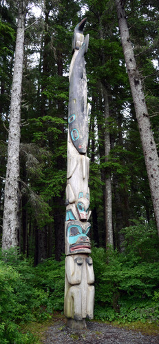 A Northwest Coast totem pole. The bottom figure appears to be a bear, above that is a wolf, then a shark and at the top is a raven.