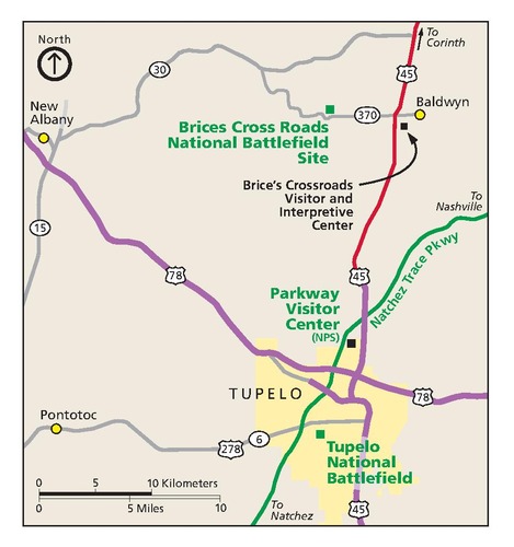 Map of Brices Cross Roads National Battlefield Site in Mississippi. This and three sites are represented with green or black squares interspersed among a web of purple, green, red, and gray roads. Tupelo, shown in yellow, is to the south, and the rest of the map is beige.