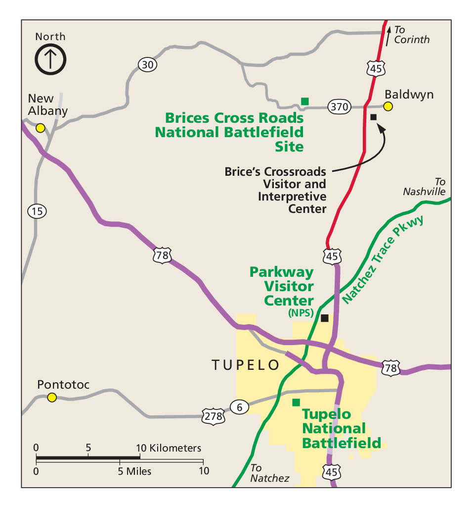Map of Brices Cross Roads National Battlefield Site in Mississippi. This and three sites are represented with green or black squares interspersed among a web of purple, green, red, and gray roads. Tupelo, shown in yellow, is to the south, and the rest of the map is beige.