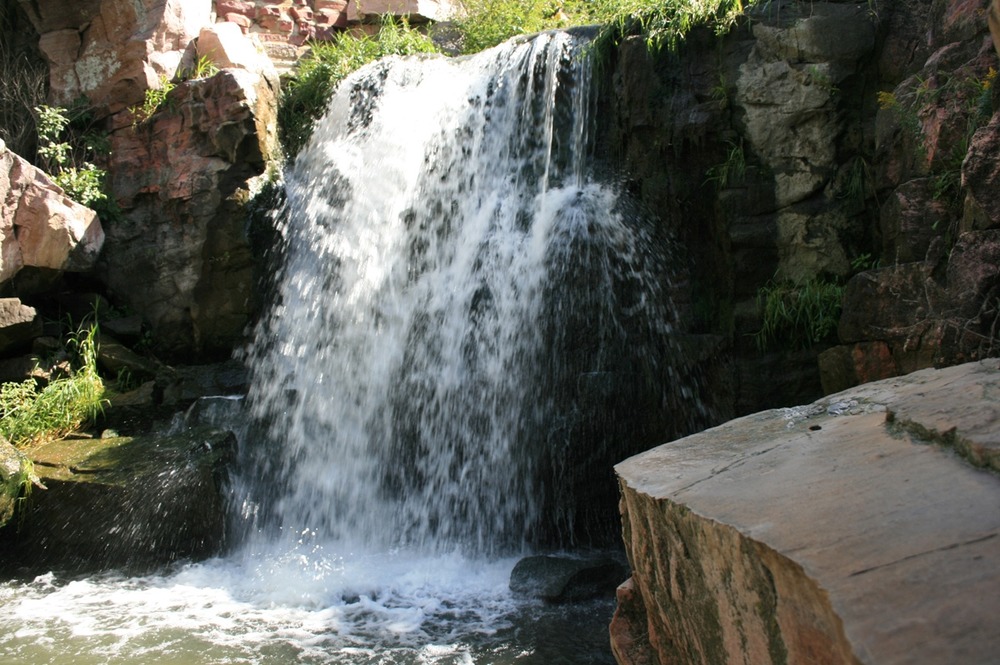 Waterfall on a sunny day surrounded by vegetation and pink cliffs