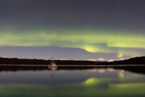 Green aurora stretches across the sky over mountains and a boat.