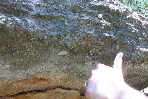 a overhang of rock in the background with a person sticking up their thumb in the foreground. 
