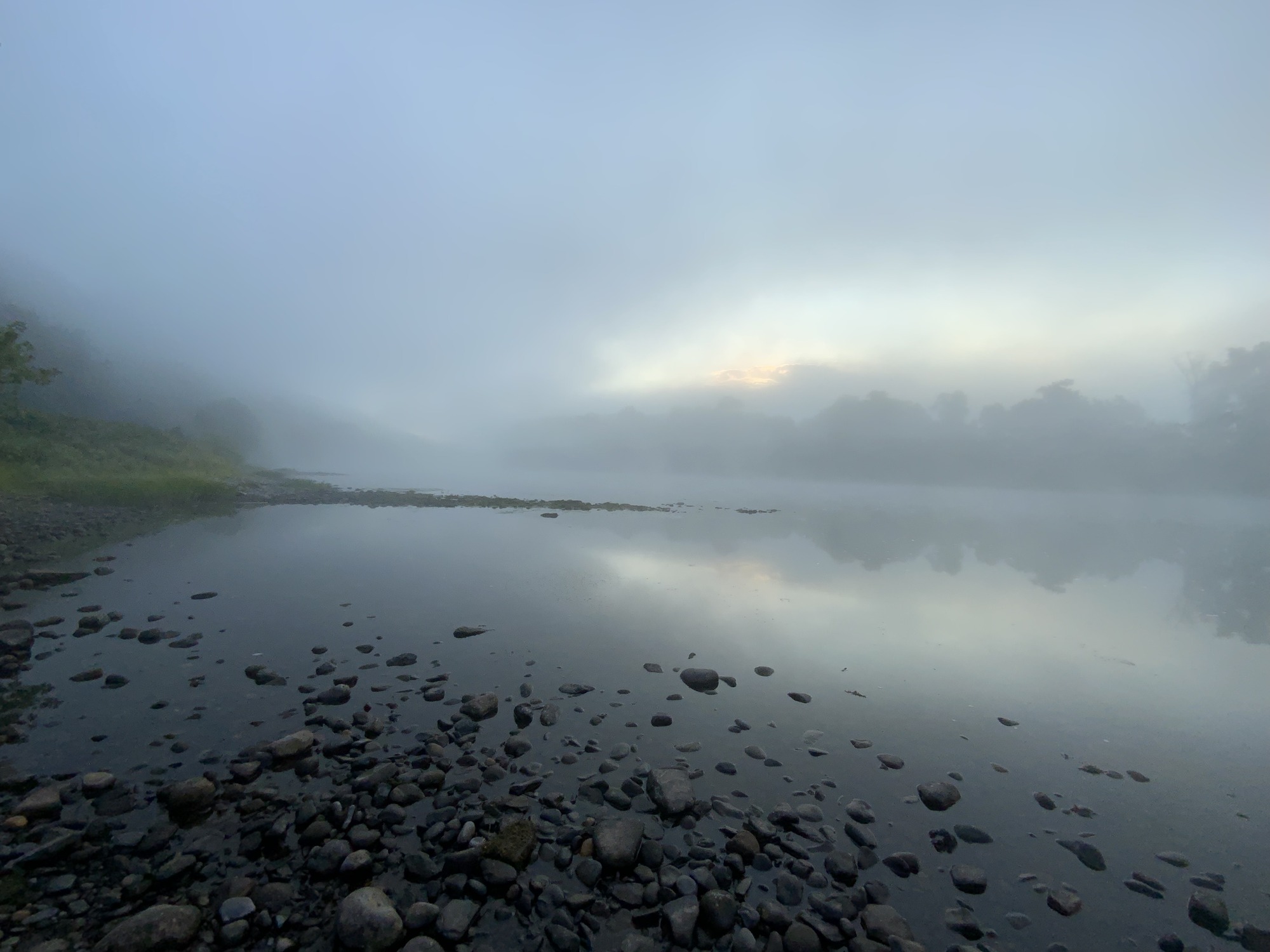 A foggy river with river stones in the foreground.