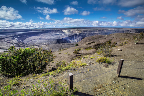 A non-erupting volcanic crater is seen from behind post and cable barriers at the edge of a cliff. 