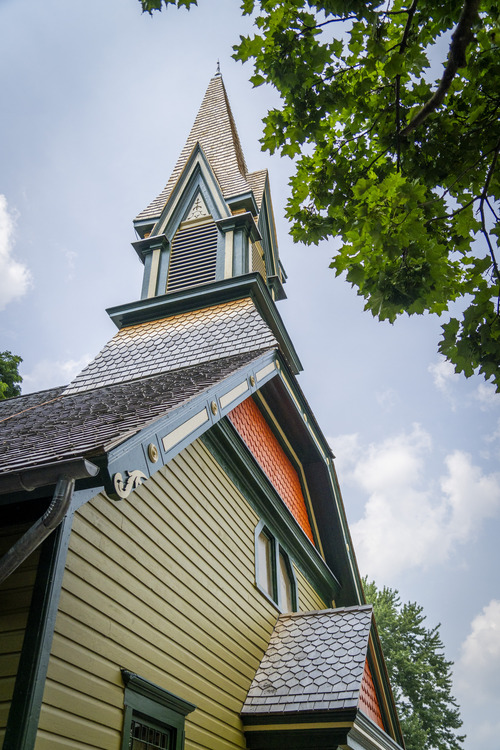 A tall church steeple, painted with green, orange, and yellow, against a blue sky with a tree to the side.