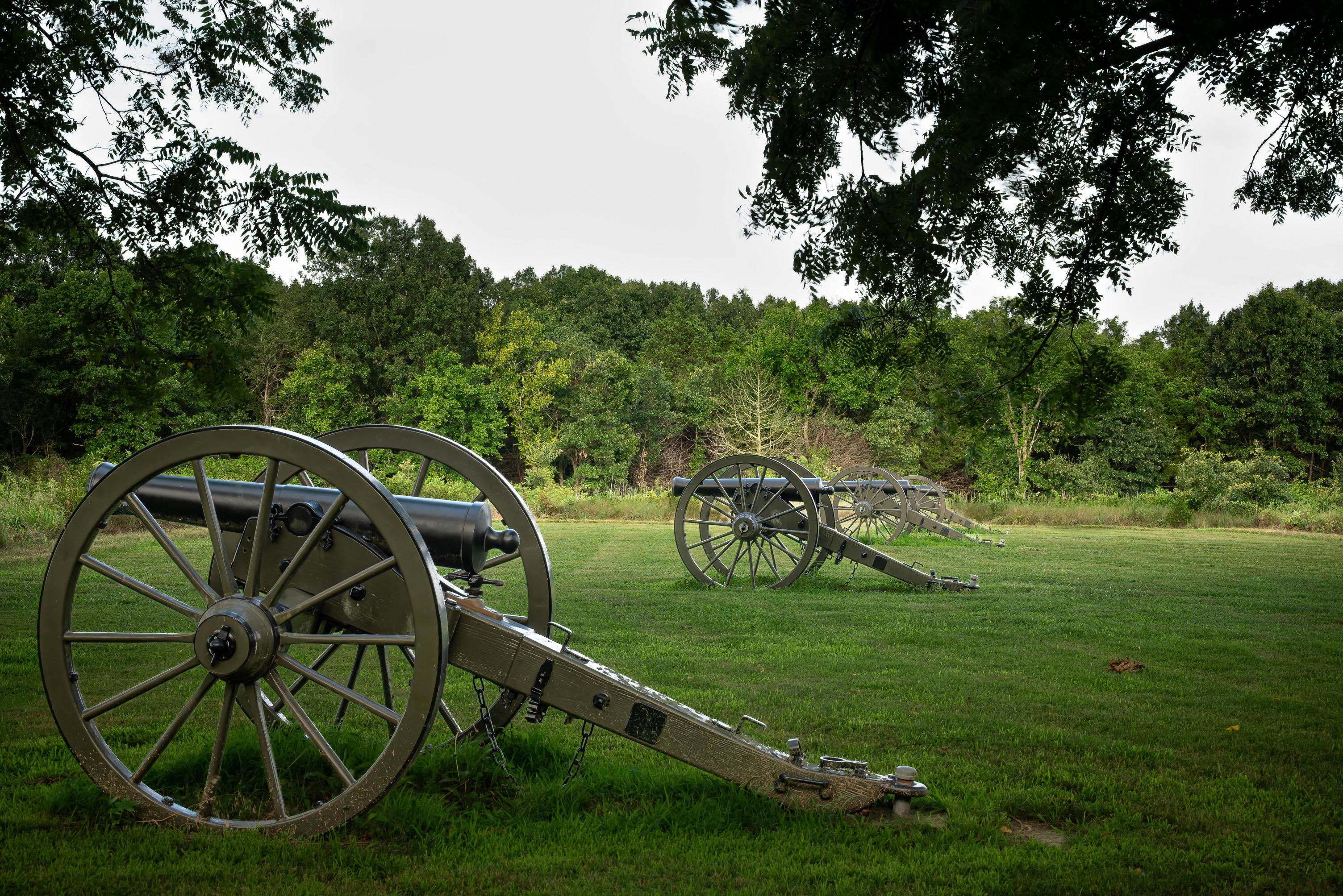 Three black artillery pieces sit on a mowed, green lawn. 