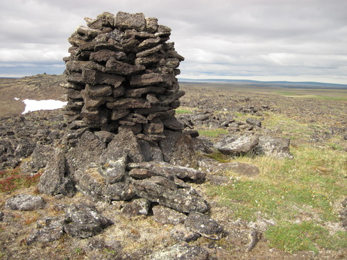Cylindrical cairn: tightly stacked slabs, nearly six feet tall on an arctic tundra, small snow field in the distance