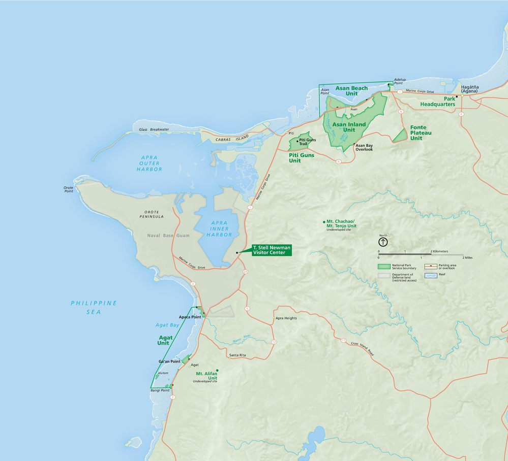 Map of a portion of the western coast of Guam including the spur-shaped Orote Peninsula. Sites are labeled in green text along the coastline and park areas are outlined in dark green against the otherwise sage-green terrain. Water is shown in blue and reefs as ice white.