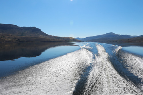 Mountains reflecting into a large body of water where a wake is crossing and creating waves
