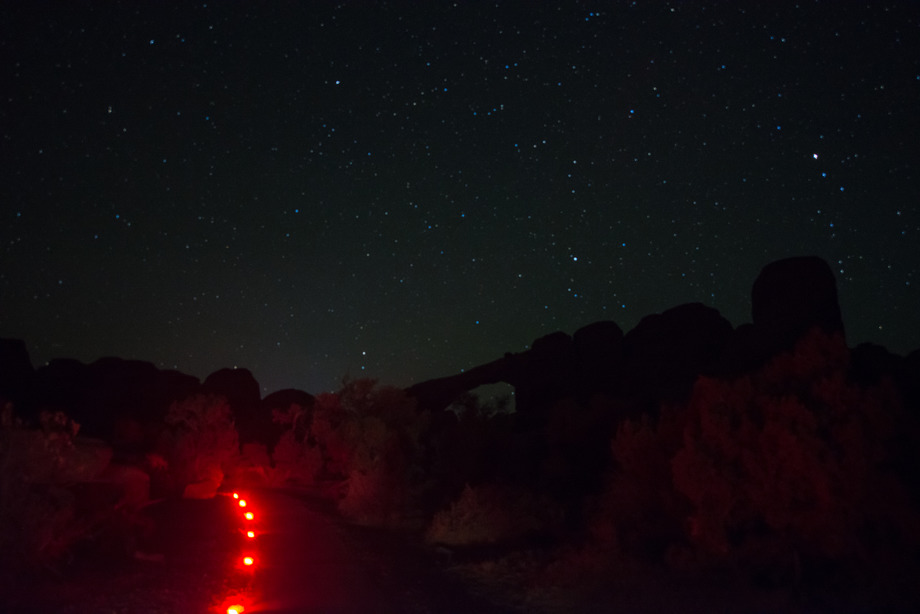 red lights line a trail with a silhouetted arch in the background