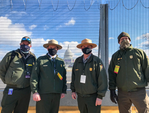 Four National Park Service employees standing next to a fence with the U.S. Capitol building in the background 