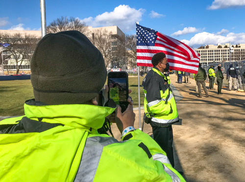 A National Park Service employee taking a picture of D.C. government employee standing next to a U.S. flag