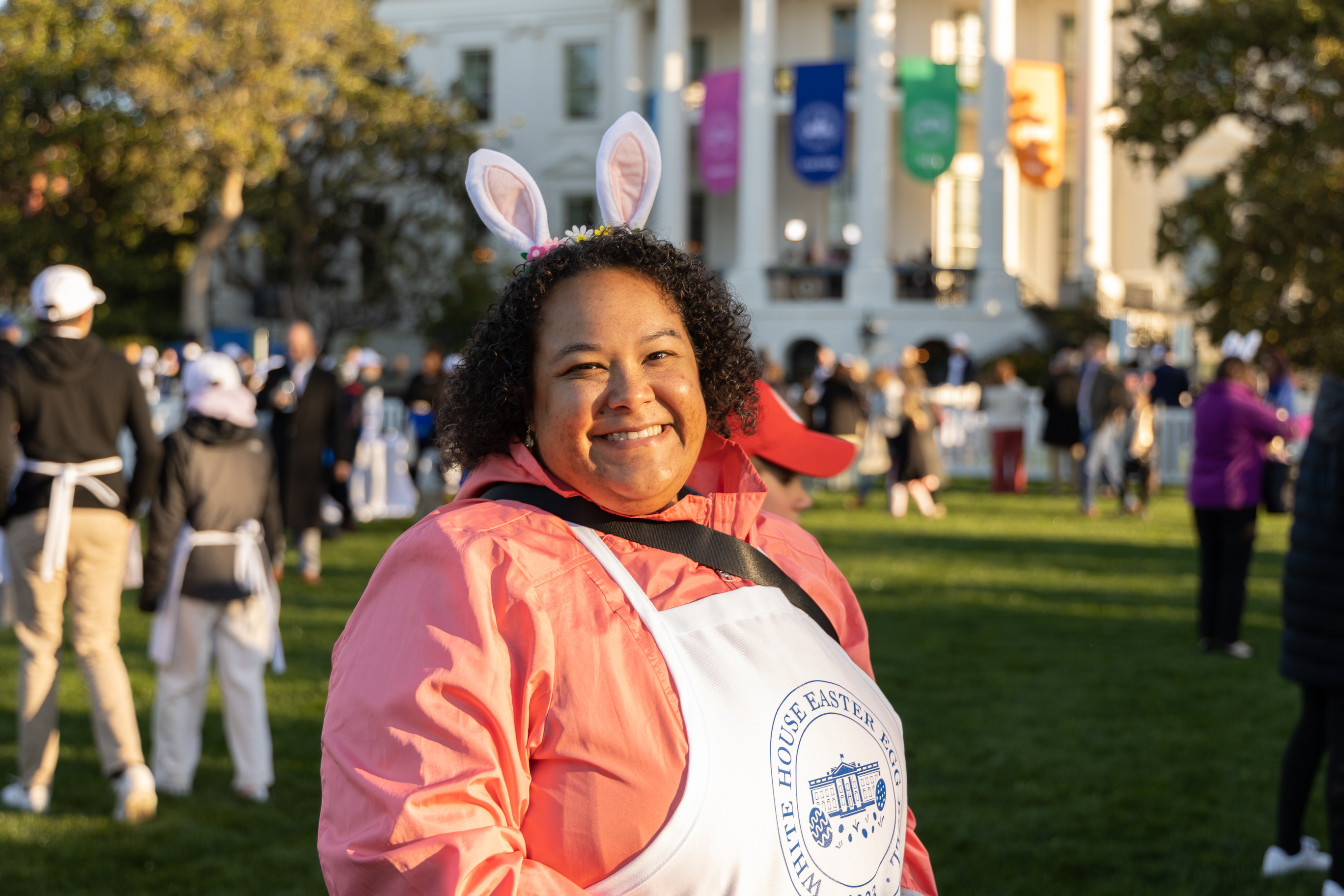 A volunteer with bunny ears smiles with the white house in the background. 