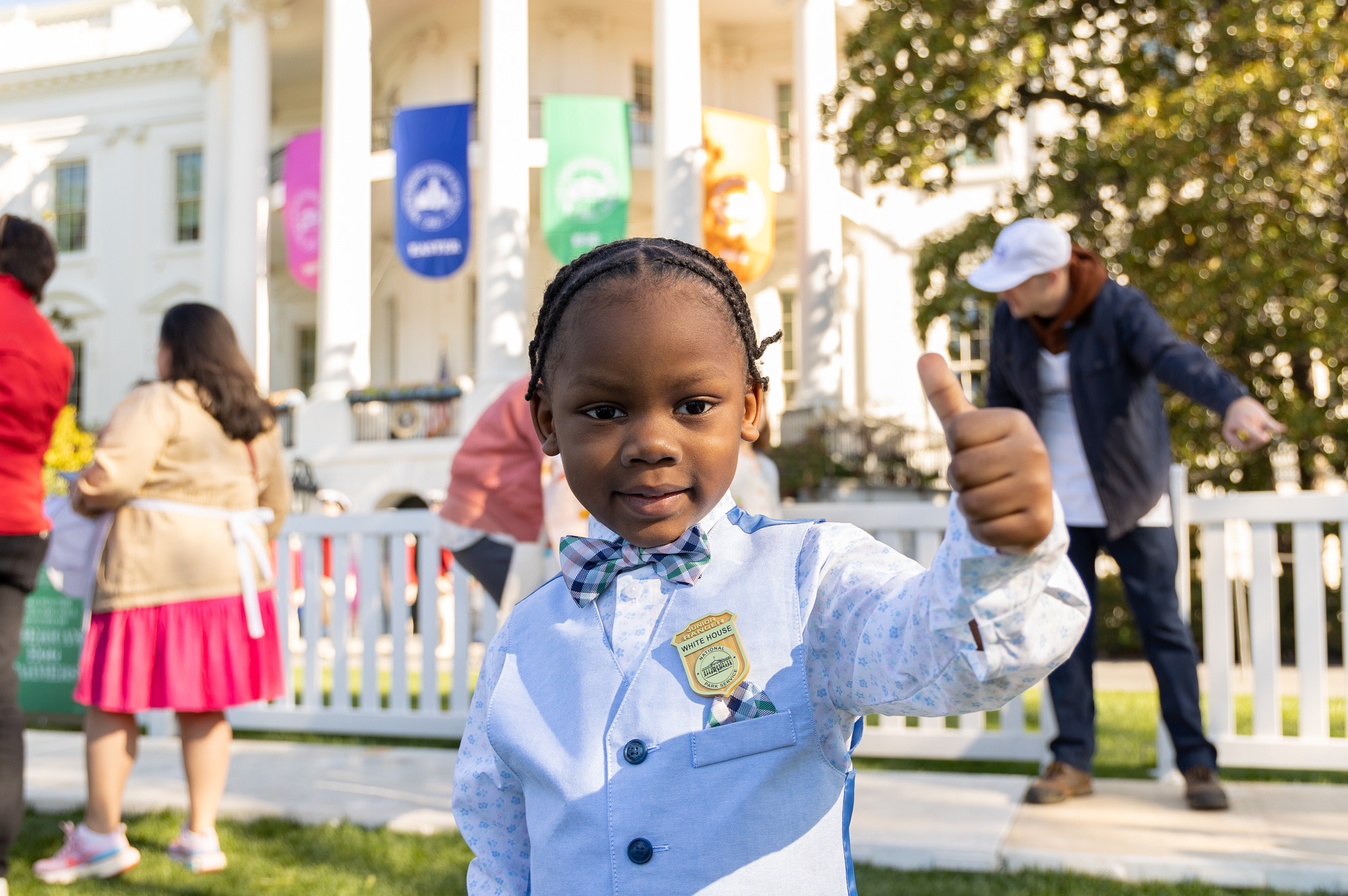 A junior ranger poses with his badge in front of the white house