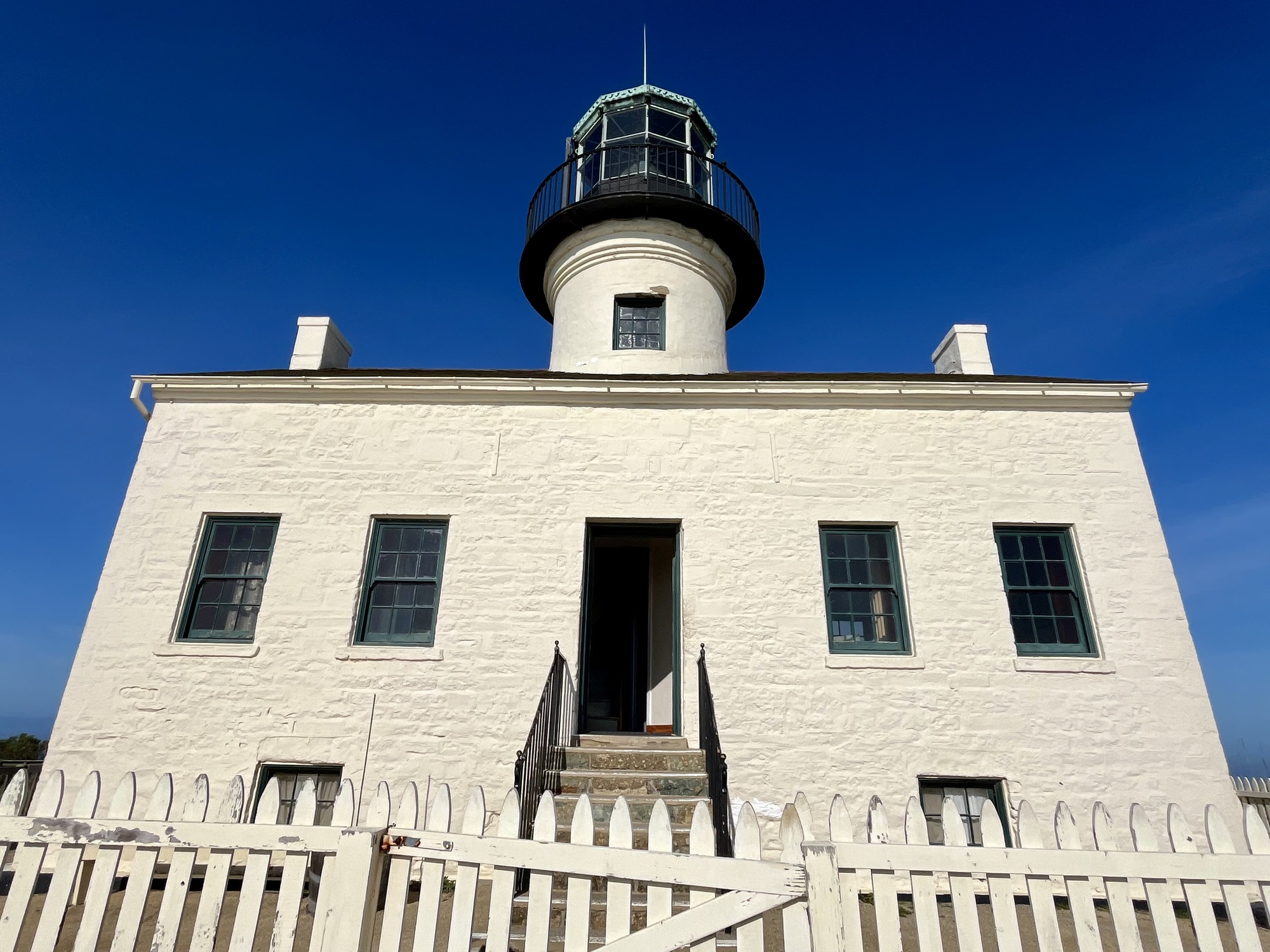 A white building with a white fence and stairs leading to a door. 