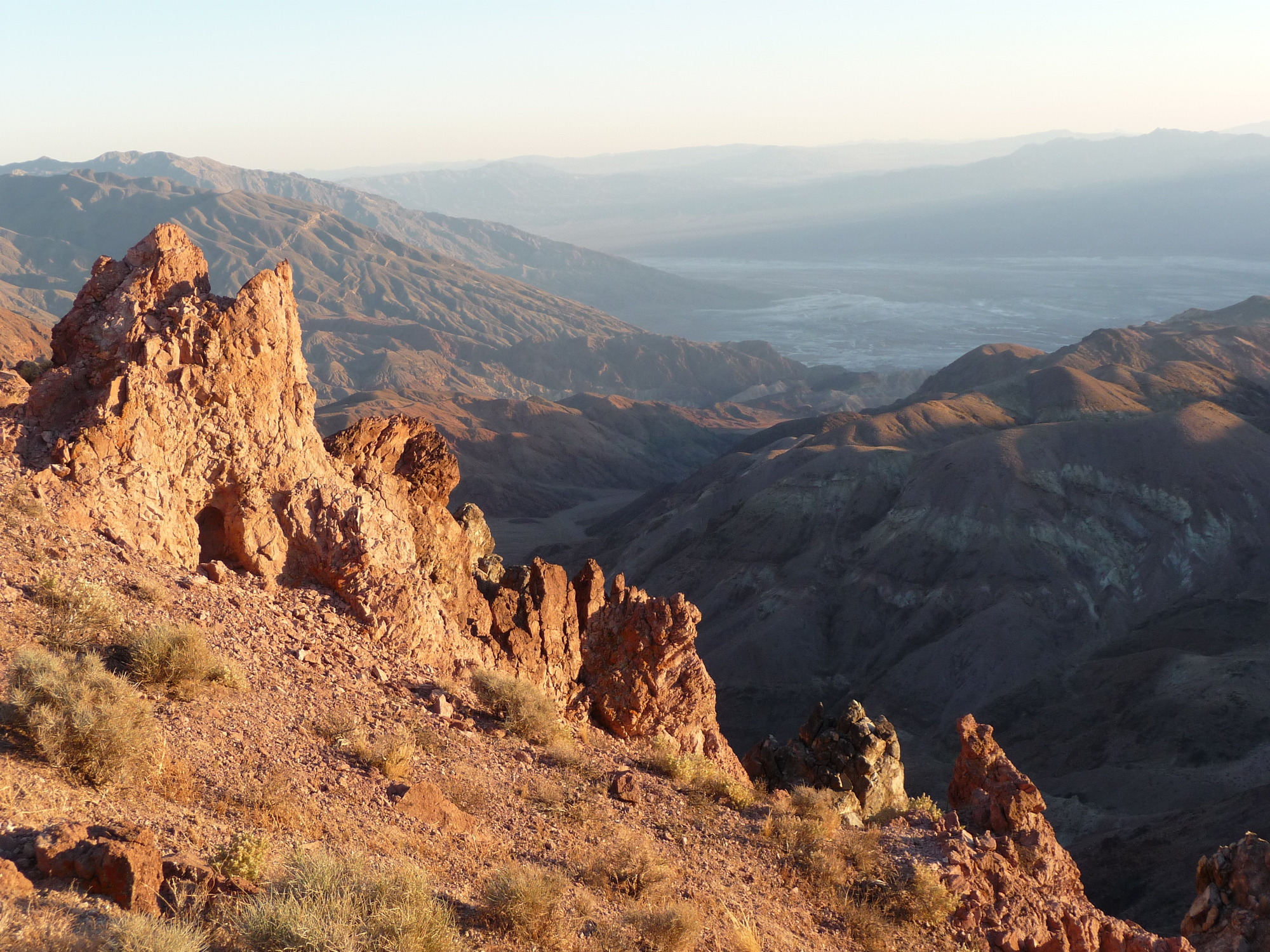 A rocky ridge on a slope, with bare hills and a broad plain with salt flats in the background.