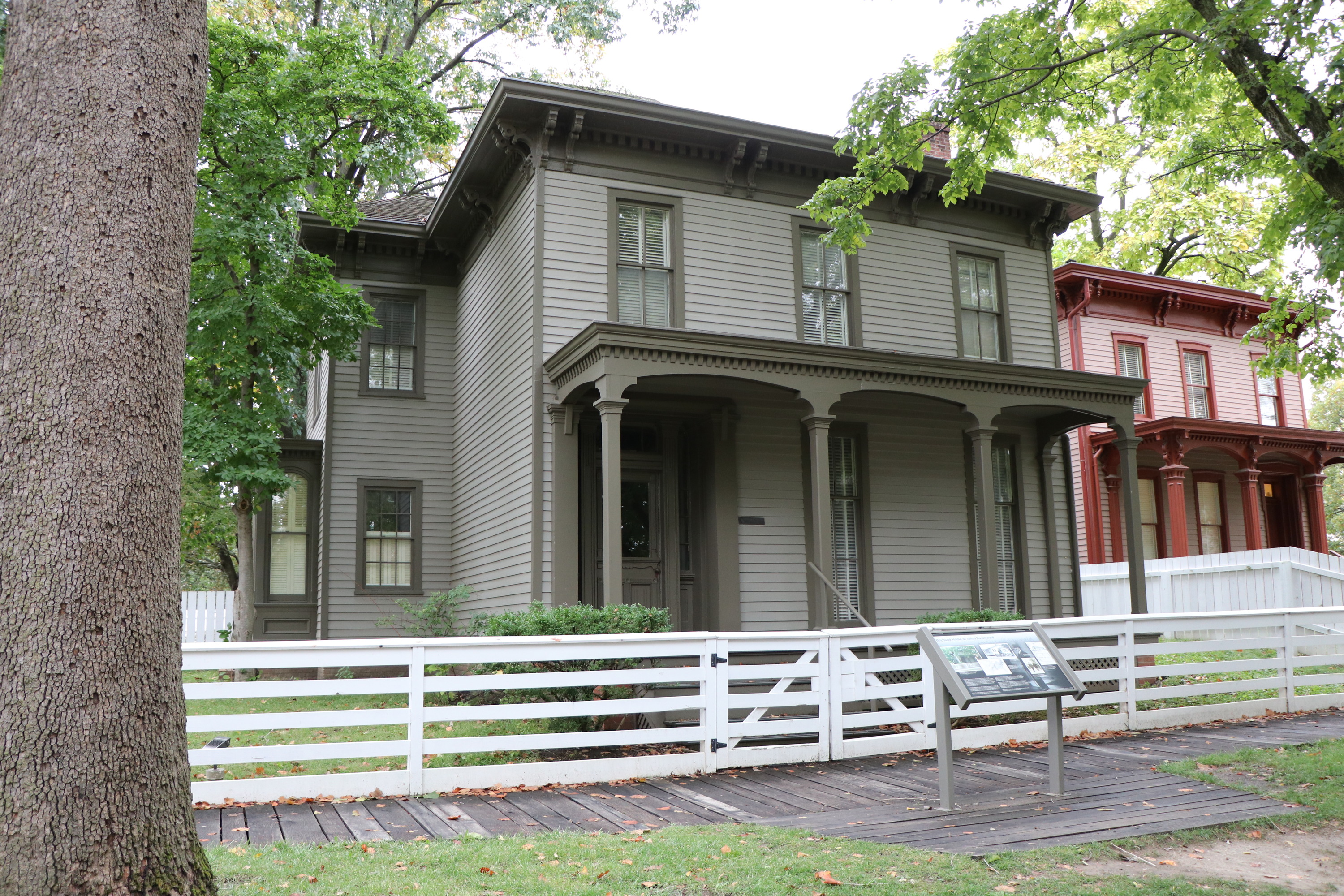 A two-story grey house with darker grey accents and a white fence in front of it.