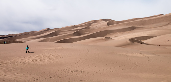 Visitors walk across the sand dunes as the sun shines. 