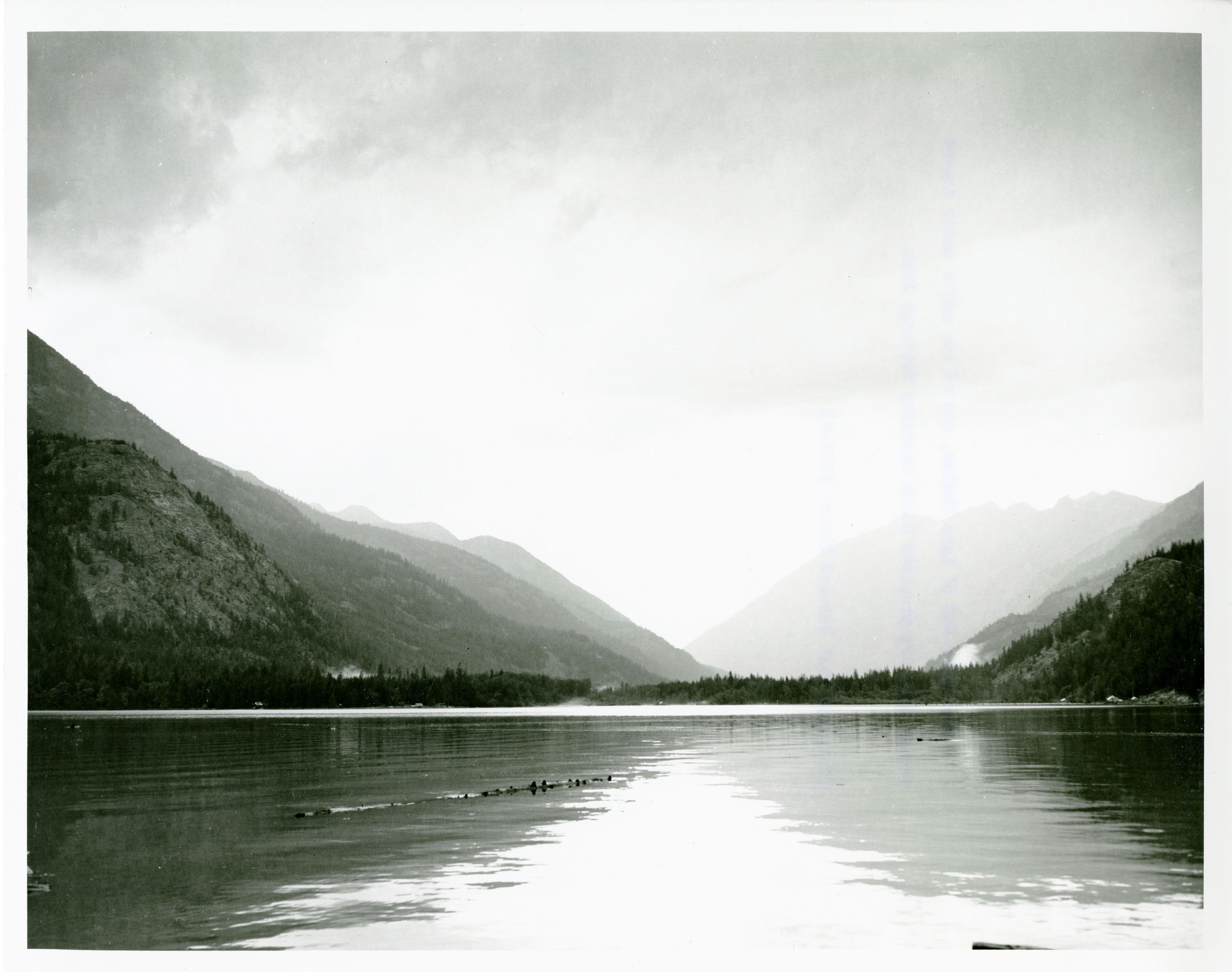 A calm lake with forested mountains in the background.