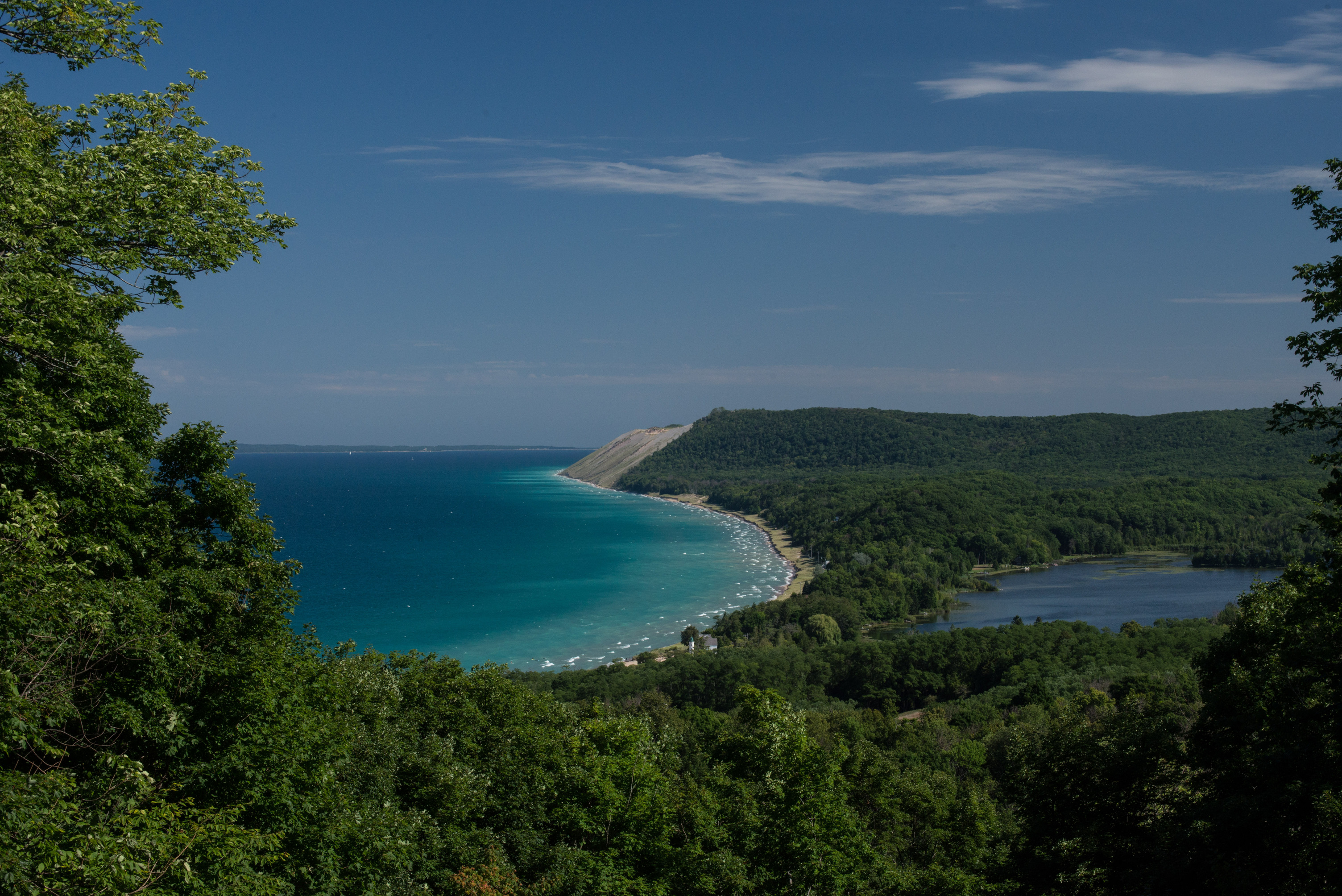 Aerial view from the Sleeping Bear Dunes bluff overlooking the turquoise waters of Lake Michigan with the Platte River inlet and forested coastline below