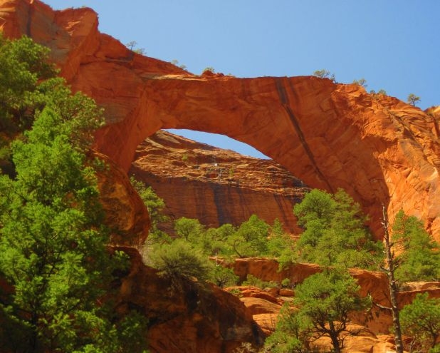 Blue sky shows through a natural arch made from red sandstone. 