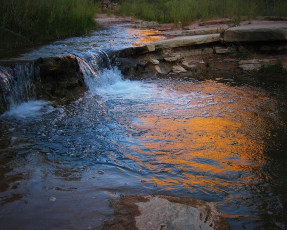 Creek water flows over a small shelf as it reflects orange light