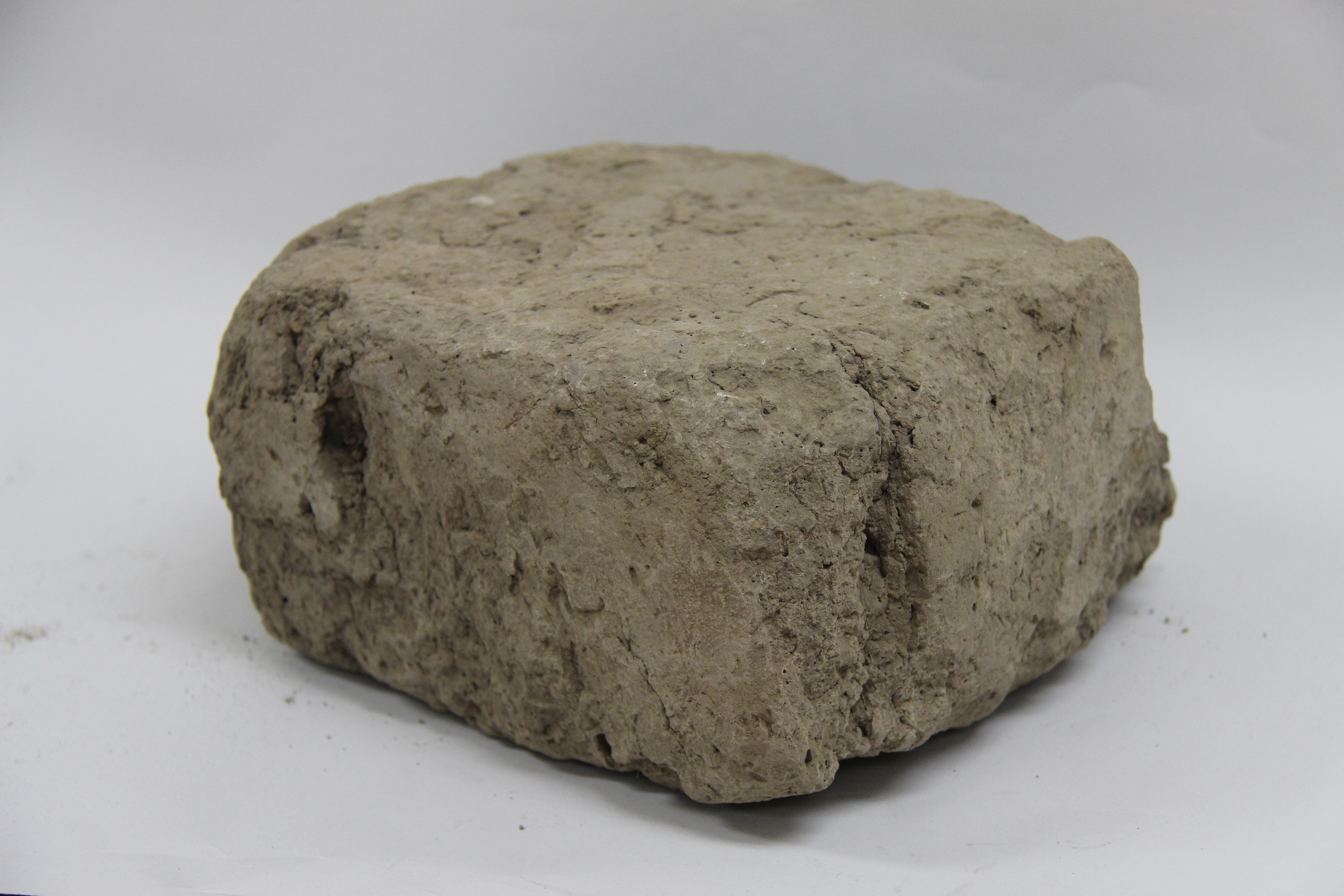 A brick made of dried mud with uneven edges rounded with wear