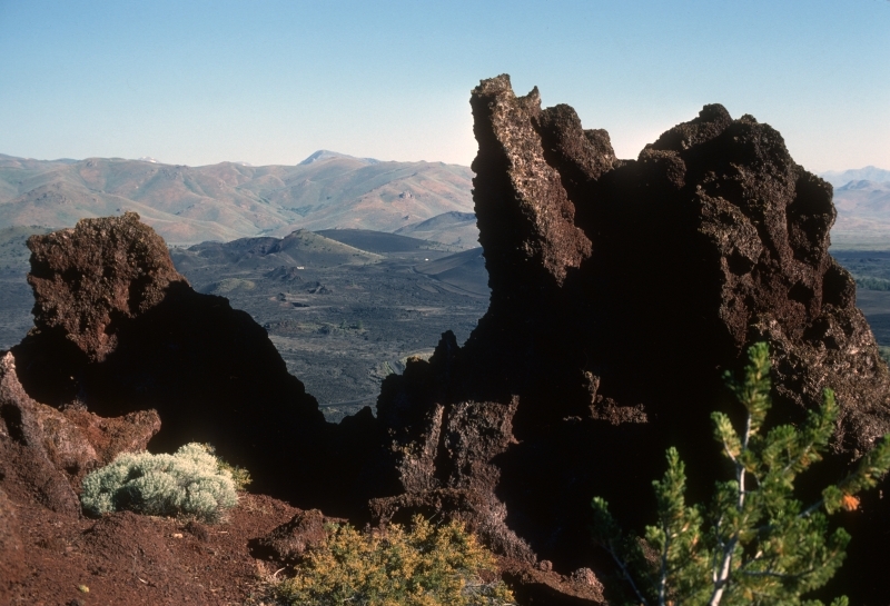 reddish brown rock outcrop with black lava fields and mountains in the distance