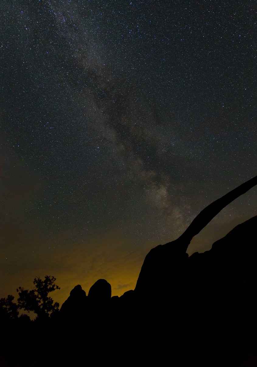 A starry sky and the Milky Way above a thin, silhouetted arch