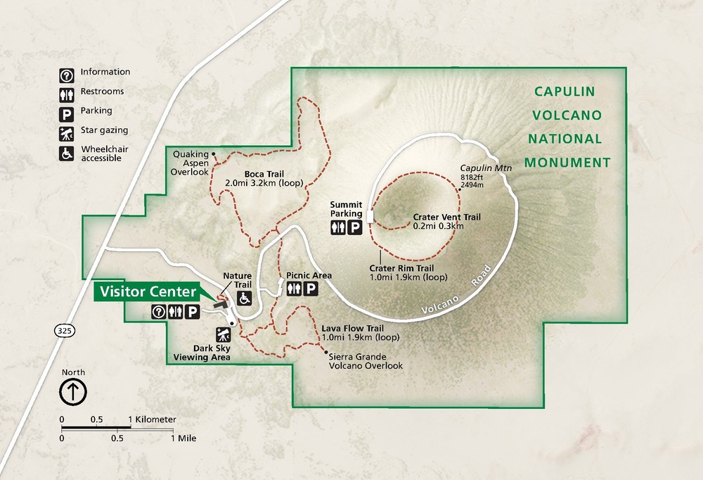 Map of Capulin Volcano National Monument in New Mexico. The park is shaded green within the dark green boundaries, which are stepped around a crater that nearly fills the park. Trails are represented by red dashed lines and a park road as a white line. The terrain around the park is beige.