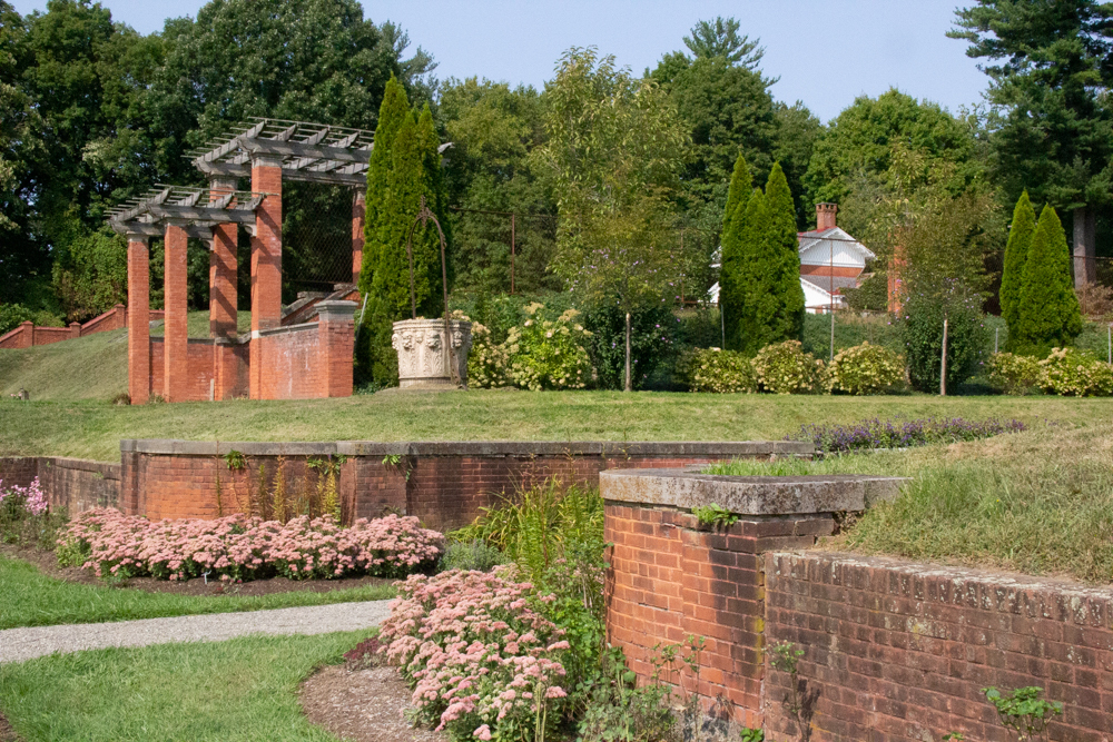 A garden with brick walls and a stone well head amidst flowering shrubs.