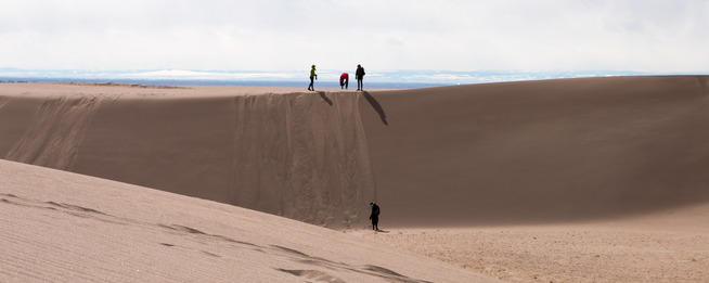 Visitors play on the top of a sand dune. 