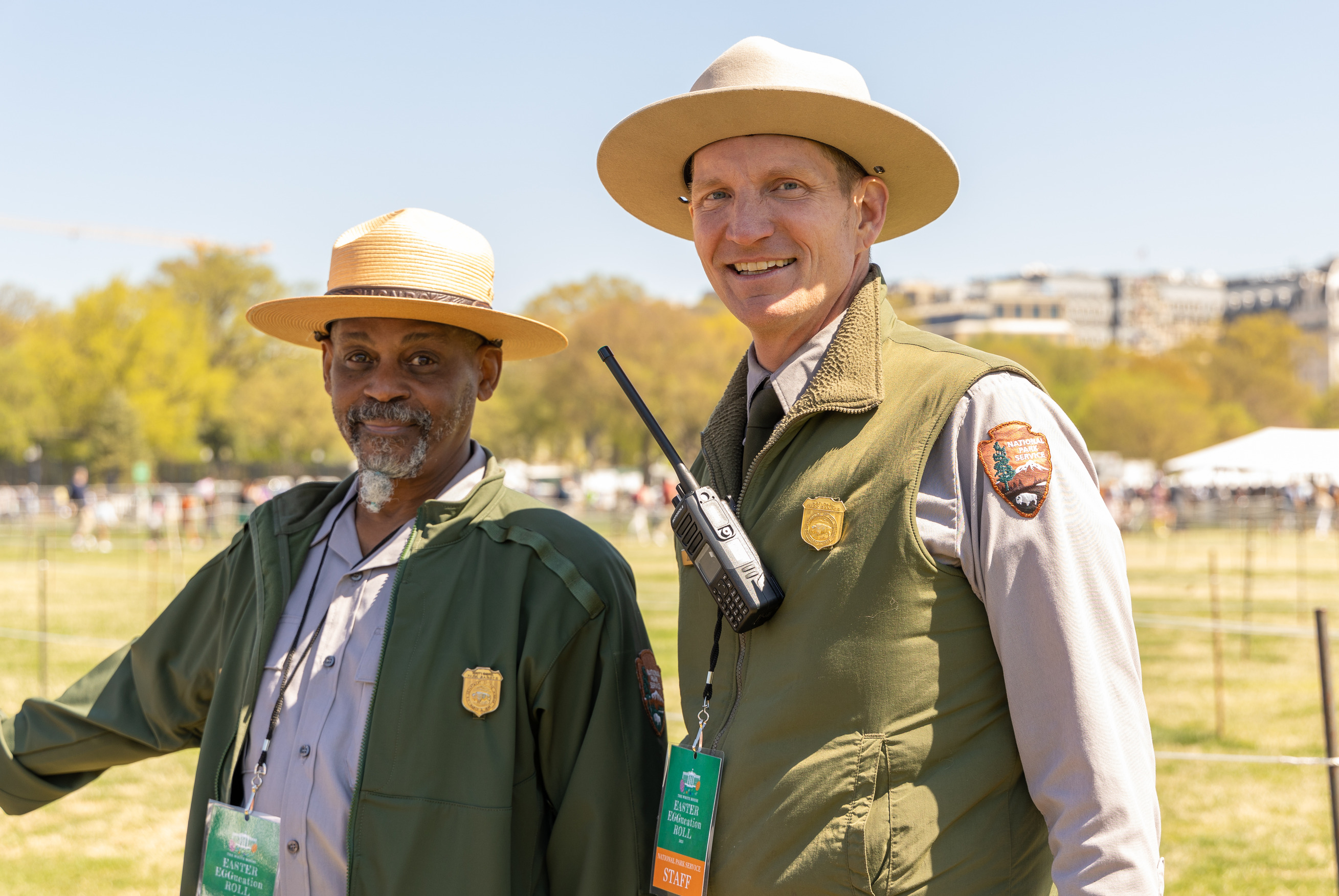 Two park rangers smile with a crowd in the distance. 