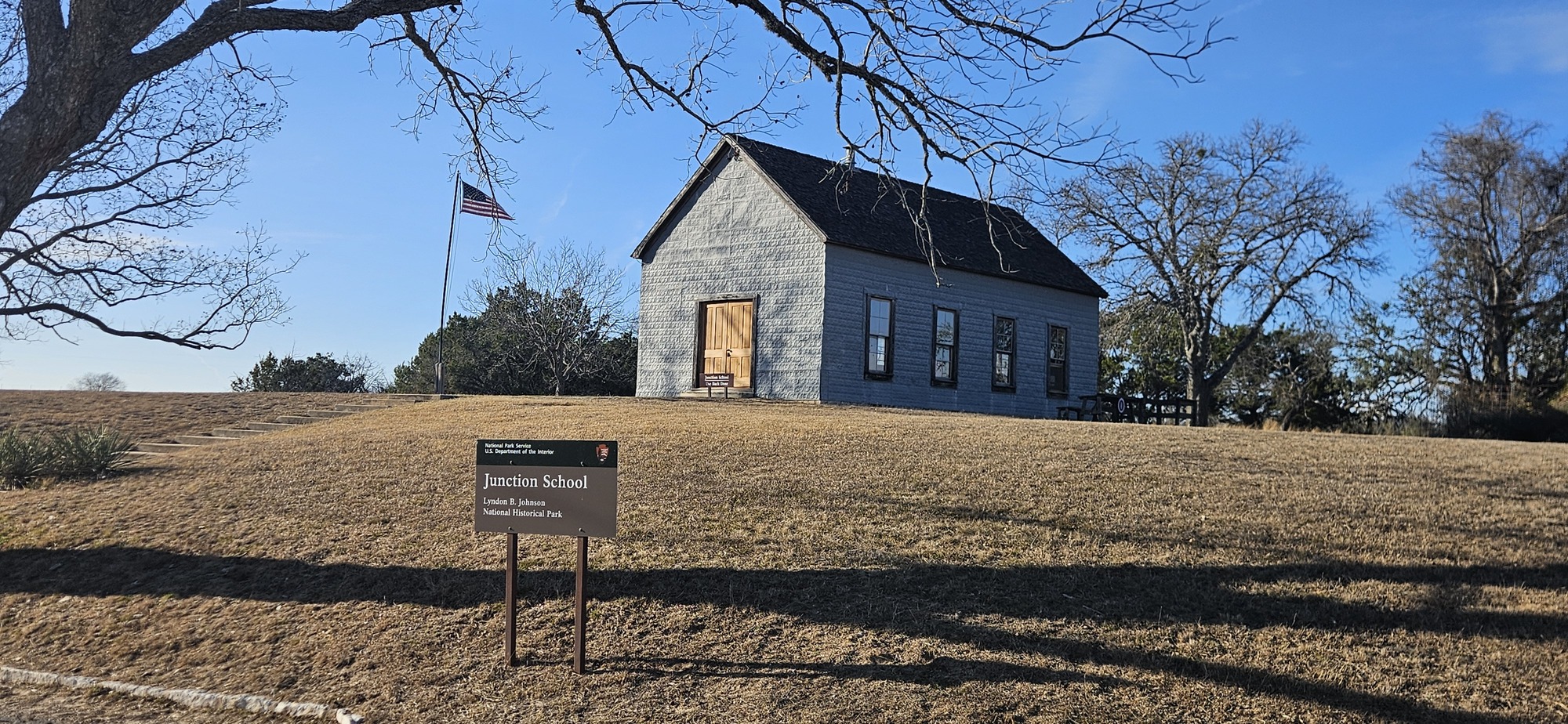 Stone building with wooden door, U.S. flag. Sign reads "Junction School."