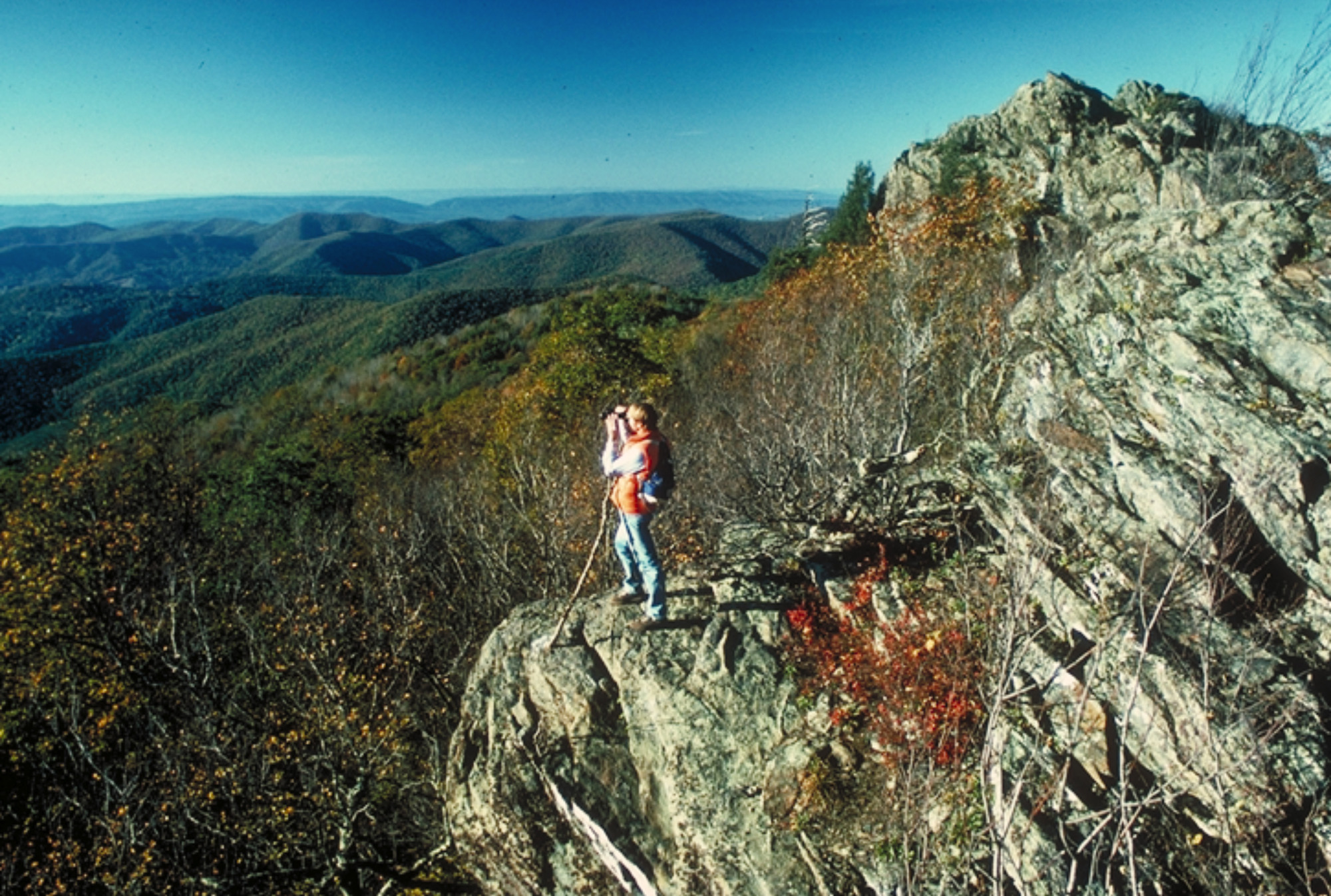 person standing on a rocky mountain ridge with peaks extending into the distance