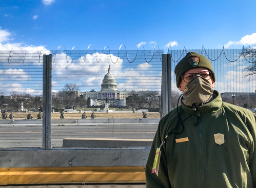 A National Park Service employee standing next to a fence with the U.S. Capitol building in the background 