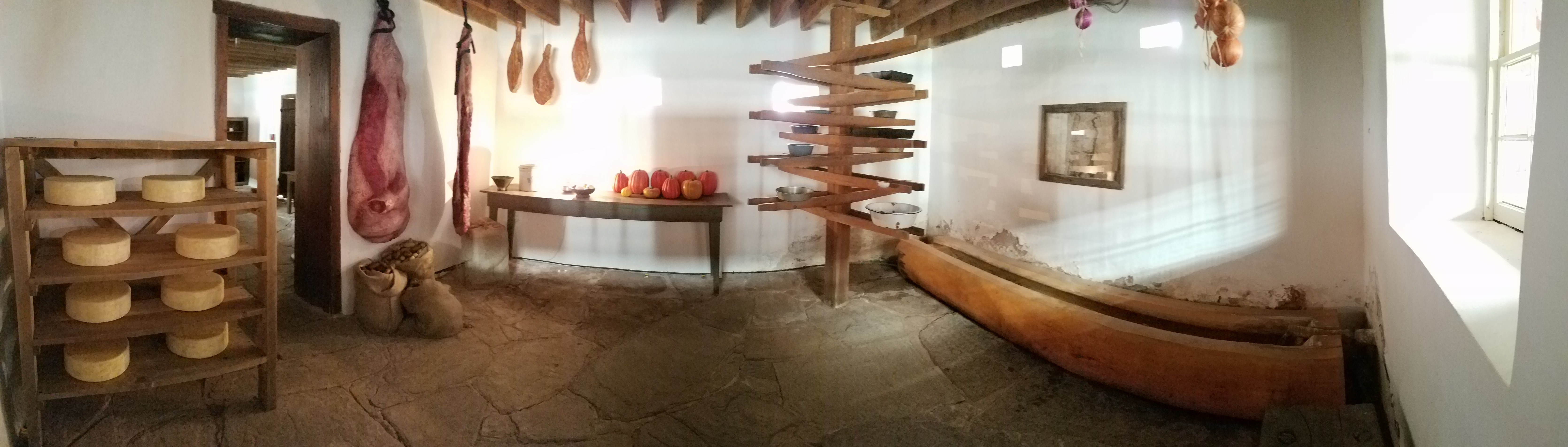 Panorama of the Spring Room, with water running through a wooden trough to the right, a lazy Susan like apparatus in the center to cool dishes, and a cheese rack to the left.