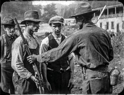 There are four men, one on the right with his back to the camera and three on the left facing the man on the right. The man on the right is a U.S. soldier. The three men on the left are coal miners and are turning over rifles to the soldier. 