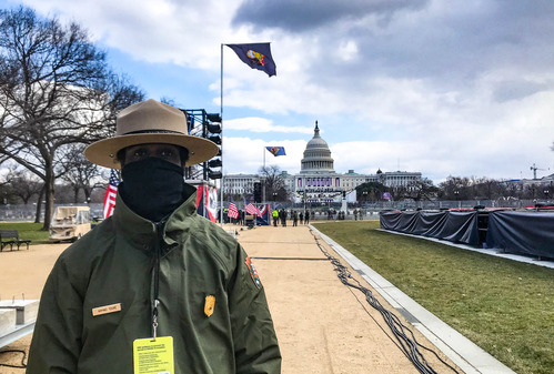 A ranger wearing a face mask standing on a wide pathway decorated with flags leading to the U.S. Capitol building