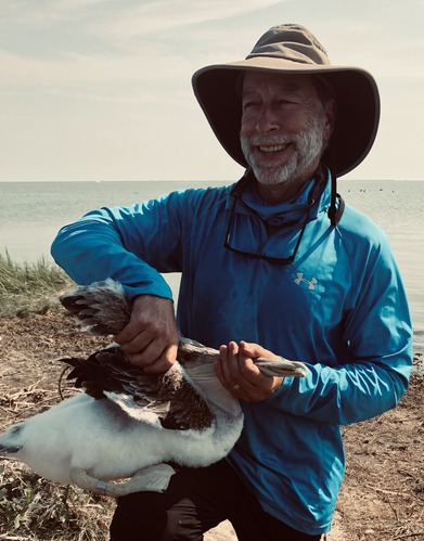 White man holding a bird in front of a body of water.