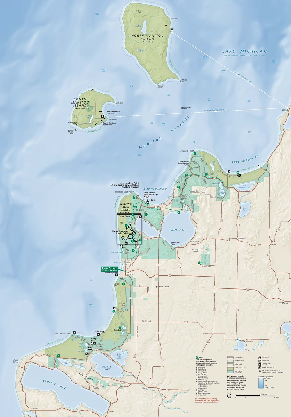 Map of Sleeping Bear Dunes National Lakeshore in Michigan. The park, shaded yellow-green and aqua-green, hooks and snakes along the bumpy curves of the pale-yellow mainland, against the tie-dye-like blue of Lake Michigan.