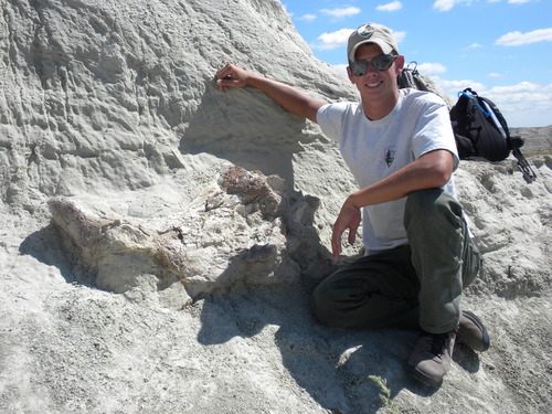 a young man posing next to a skull on the side of a cliff.