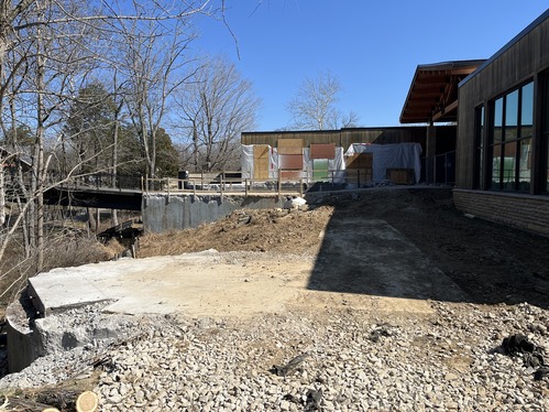 A large excavated area of dirt shows where concrete has been removed behind a large building.