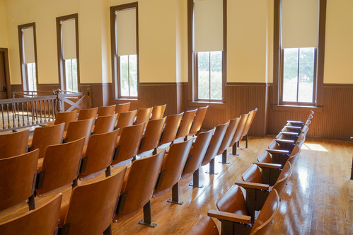 Rows of stadium-style wooden seats with sunlight coming through large windows