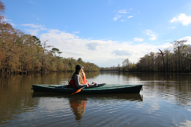 solo kayaker, with green kayak and orange paddle, enjoying the view of the wide waterway in the afternoon