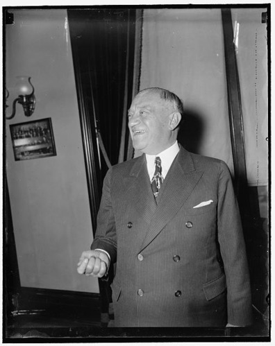 A candid photo of a middle-aged man. He is in an expensive looking suit and smiling joyfully.