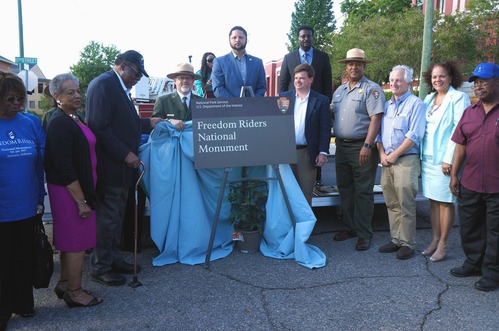 Dignitaries and presenters at celebration surrounding sign that reads "Freedom Riders National Monument"