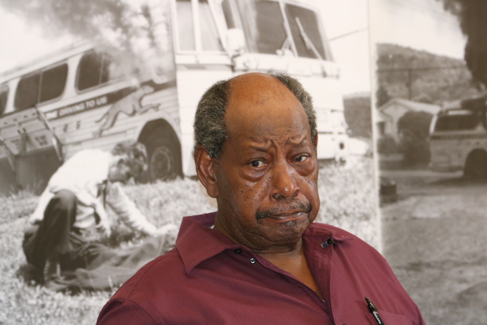 man seen from chest up wearing maroon shirt; black and white photos in background